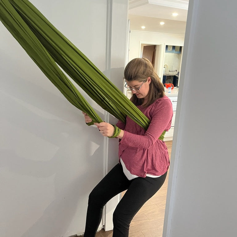 Pregnant woman using the birth sling in a doorway